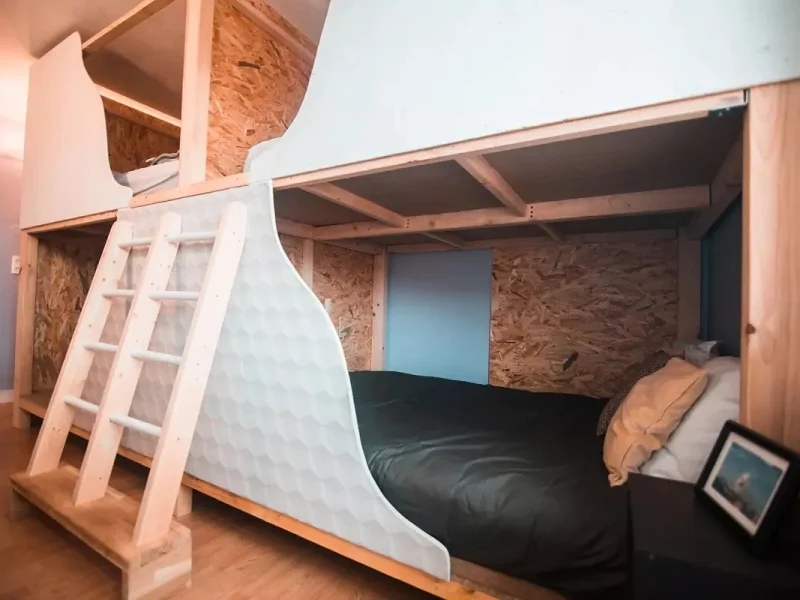 Interior view of a group accommodation room with wooden lofted bunk beds and white ladder access at Surfbase Vieux-Boucau.