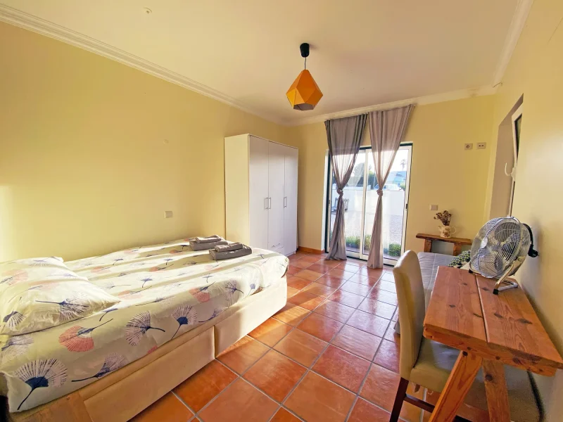 Doppelzimmer im Mayla Surf House mit Terrakotta-Fliesenboden und Zugang zur Terrasse über Glastüren.