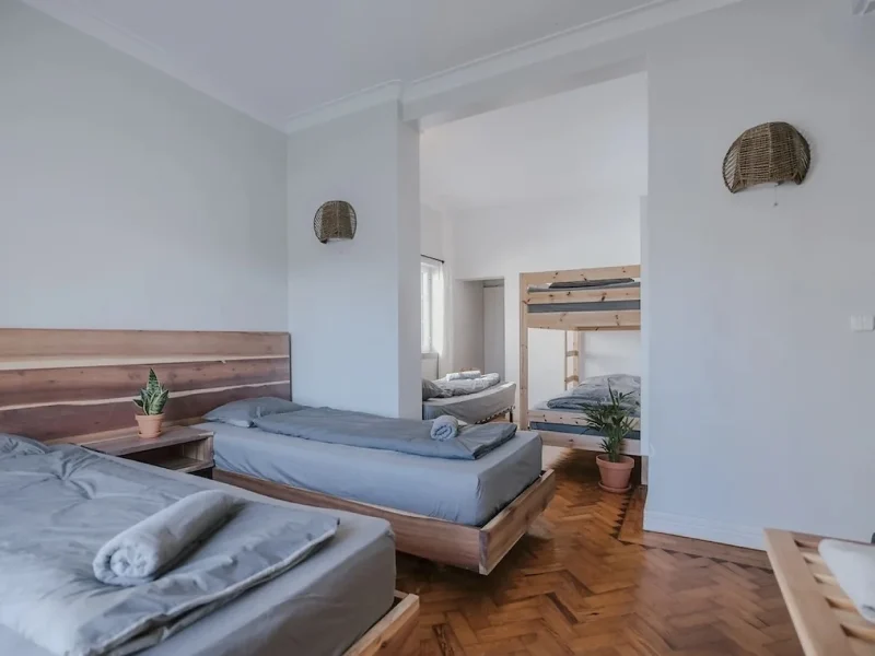 Multi-bed dormitory room at SURFinn Lisbon with wooden frame beds, potted plants, and white walls.