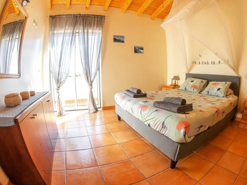 Odeceixe-Deluxe-Schlafzimmer im Mayla Surf House mit Queen-Bett, Terrakottaboden und Terrassenzugang.