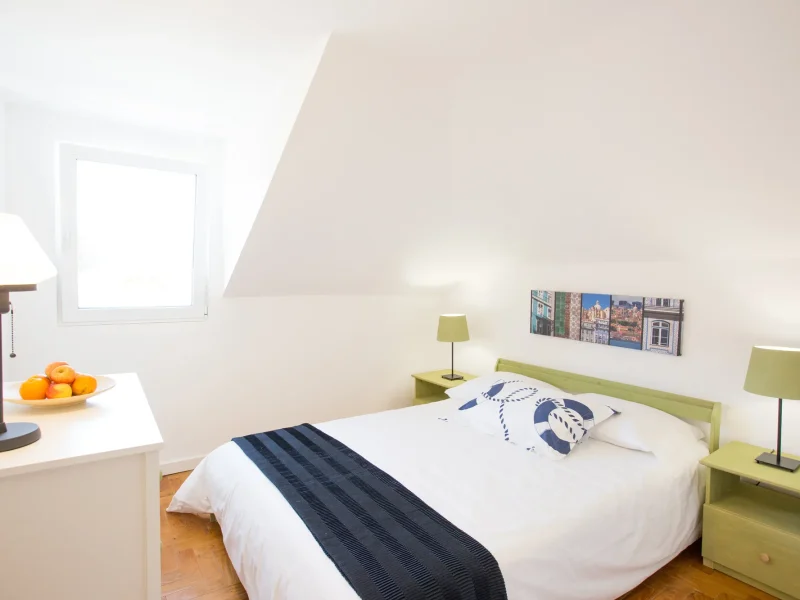Private bedroom with double bed, green bedside table, lamp, and nautical-themed pillow in attic room.
