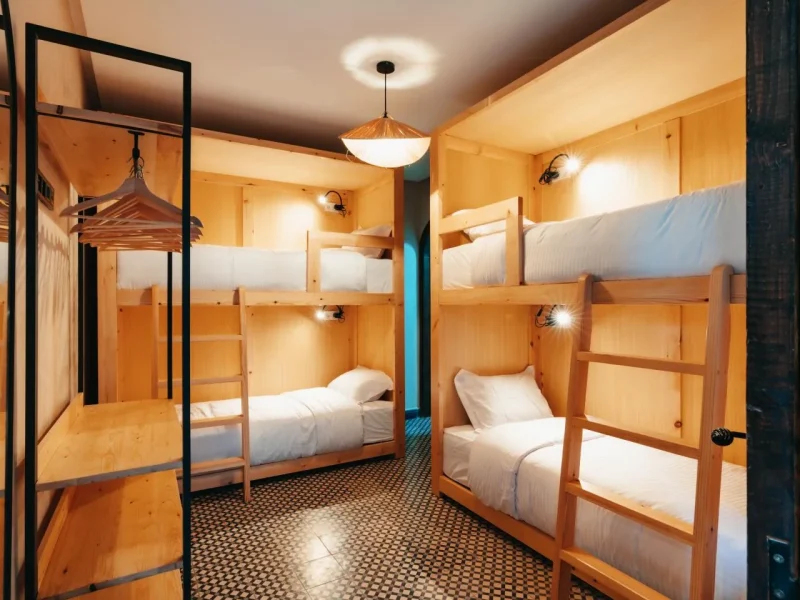 Female shared dormitory room with six wooden bunk beds, white linens, and patterned tile flooring at Gota Dagua Tamraght.