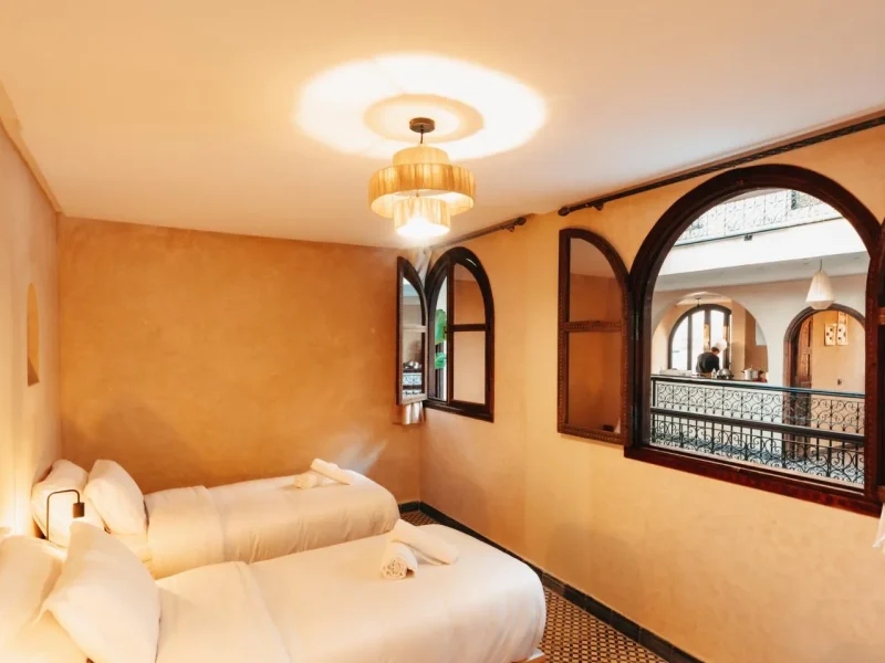 Twin beds with white linens in a private guest room with warm orange walls and dark wood archways.