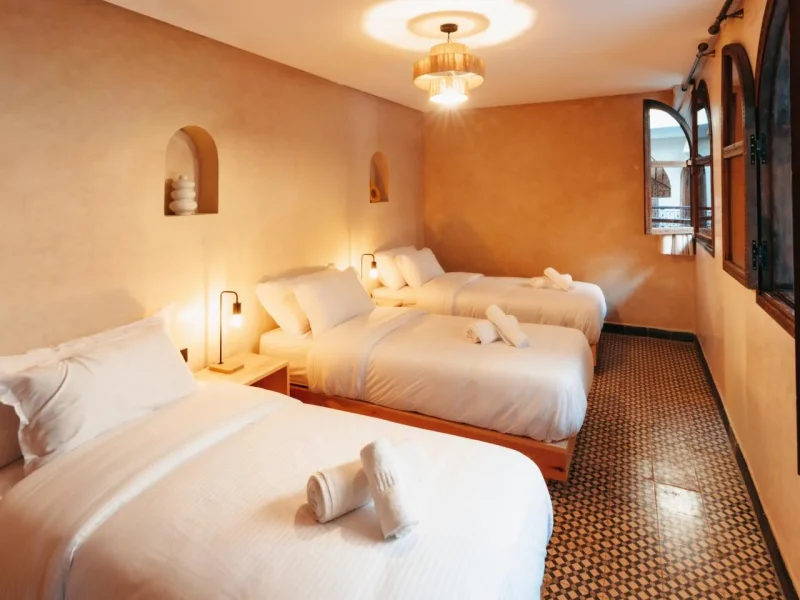 Multi-bed accommodation room at Gota Dagua Tamraght with three twin beds, arched wall alcoves, and ocean view through window.