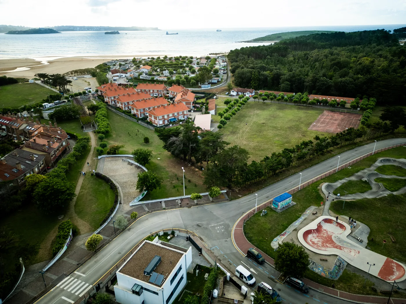 Aerial view of Surfbase Loredo in Cantabria showing the main building with orange roofing, surrounding sports facilities, and nearby beach.