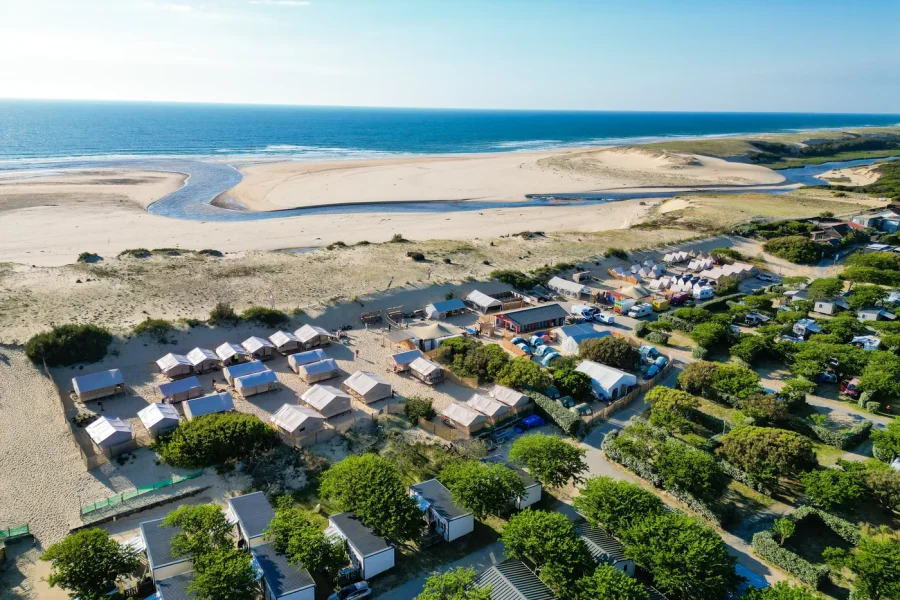 Aerial view of SURFblend Moliets surf camp with white-roofed accommodations, river estuary, and sandy beach with breaks in Moliets, France.