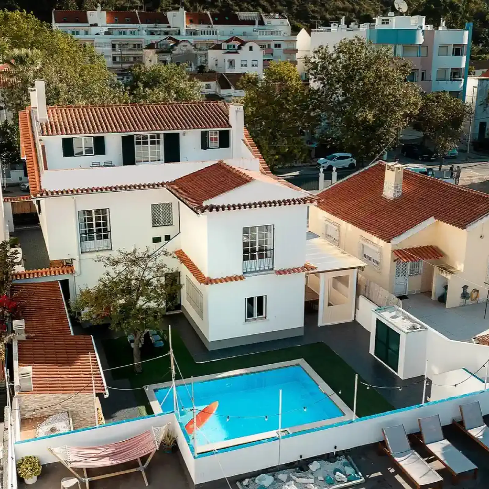 Vue aérienne de la propriété SURFinn Lisbon montrant villas blanches avec toits en terracotta, piscine bleue et bâtiments résidentiels environnants.
