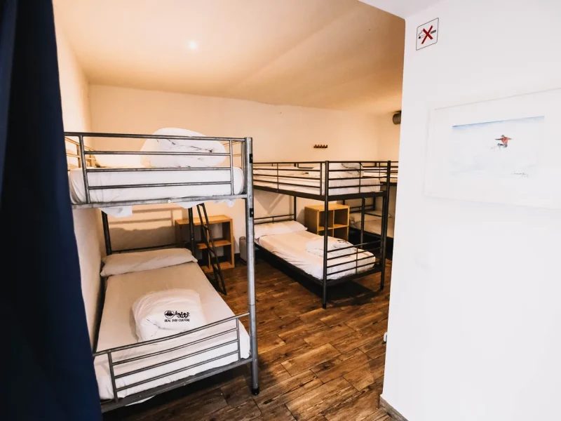 Chambre dortoir partagée avec plusieurs lits superposés métalliques et parquet en bois à Surfbase Loredo, Cantabrie.