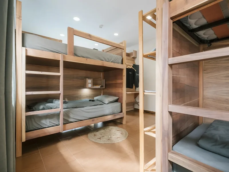 Multiple wooden bunk beds with integrated shelving and personal lighting in a shared dormitory room at SURFinn Lisbon.