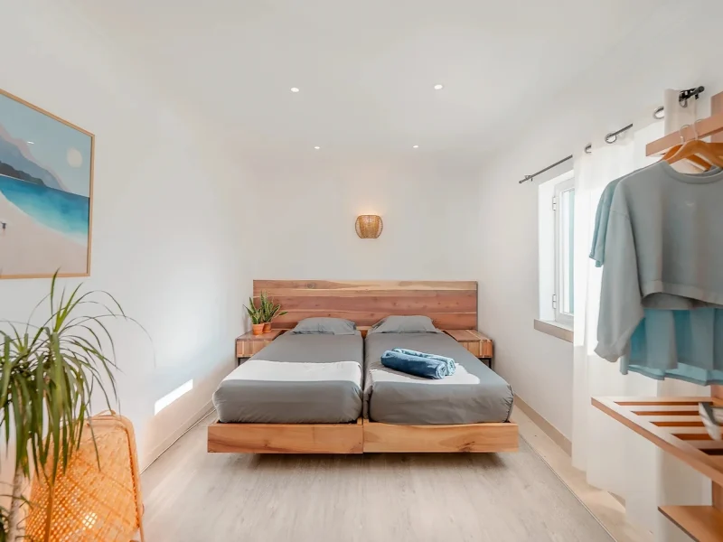 Twin single beds with natural wood frame and headboard in a minimal bedroom at SURFinn Lisbon, Portugal.