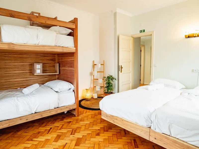 Four Deluxe room featuring wooden bunk bed with white linens and single bed on herringbone wood flooring.