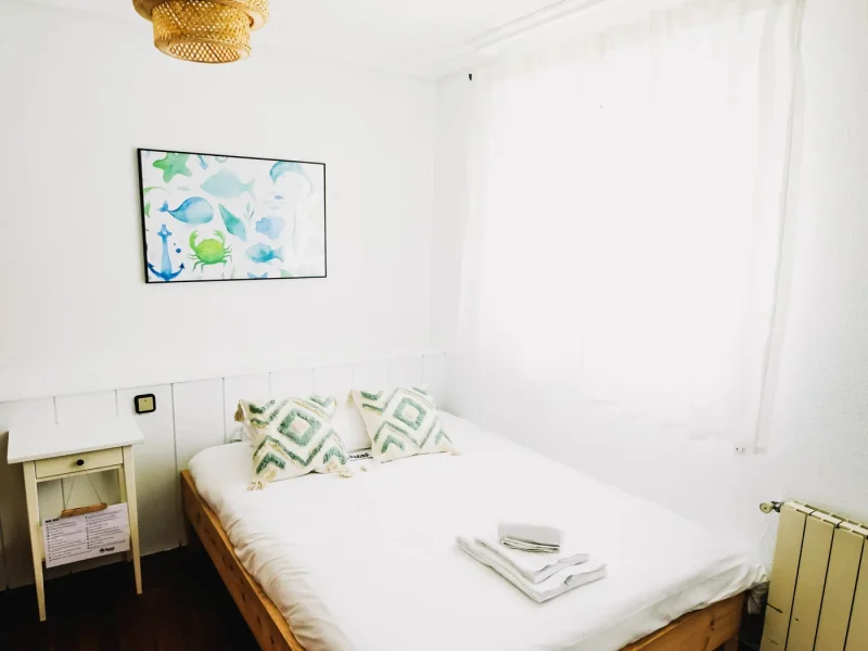 Chambre avec lit simple, table de chevet en bois, lampe tissée au plafond et œuvre murale sur le thème de l'océan à Surfbase Loredo en Cantabrie.