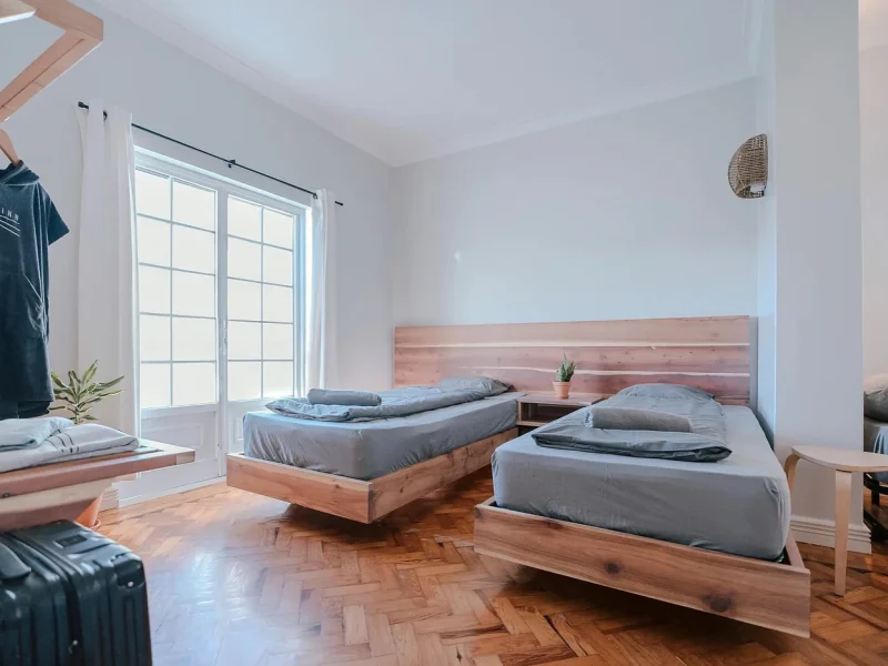 Twin bedroom in SURFinn Lisbon's Royal Five room with wooden bed frames and light gray bedding.