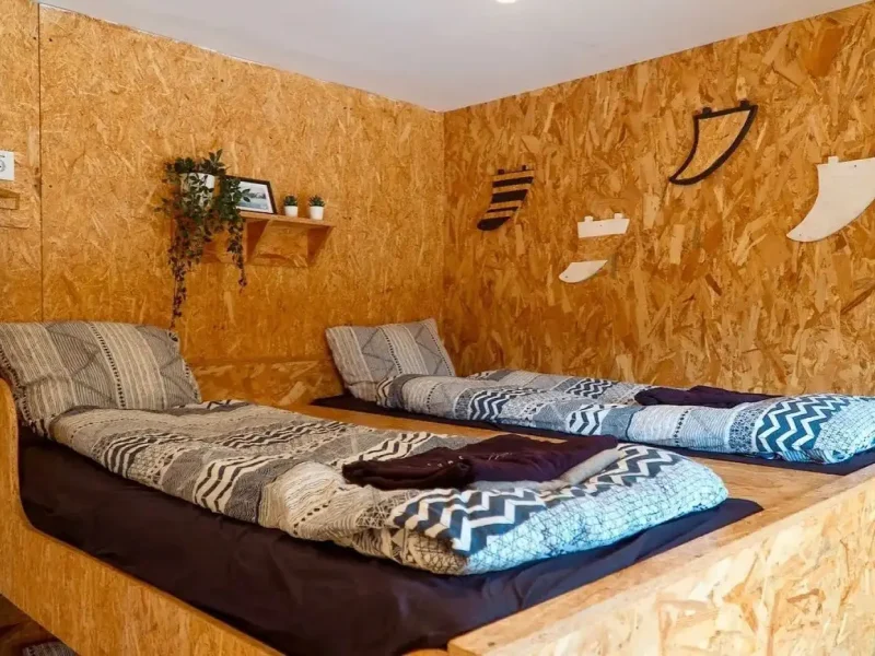Shared dorm room with cork walls, low platform beds with patterned bedding, and wooden shelving at SURFinn Vieux-Boucau.
