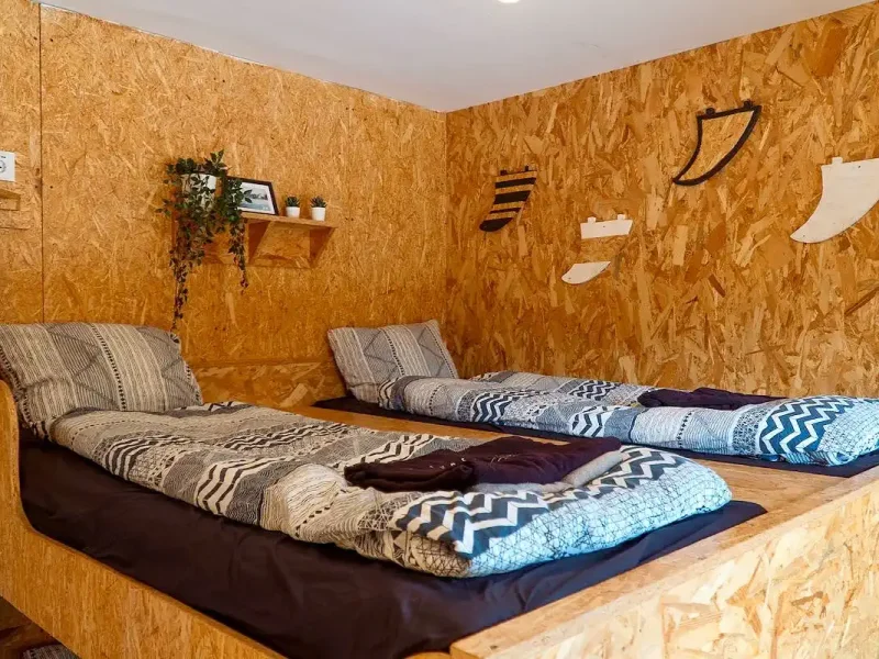 Shared dormitory room at SURFinn Vieux Boucau with cork walls, ground-level mattresses, and geometric patterned bedding.