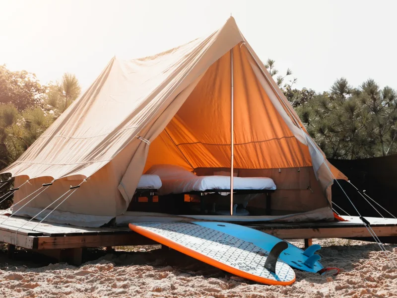 Cream and orange bell tent accommodation at SURFblend Moliets with surfboard propped outside on sand.