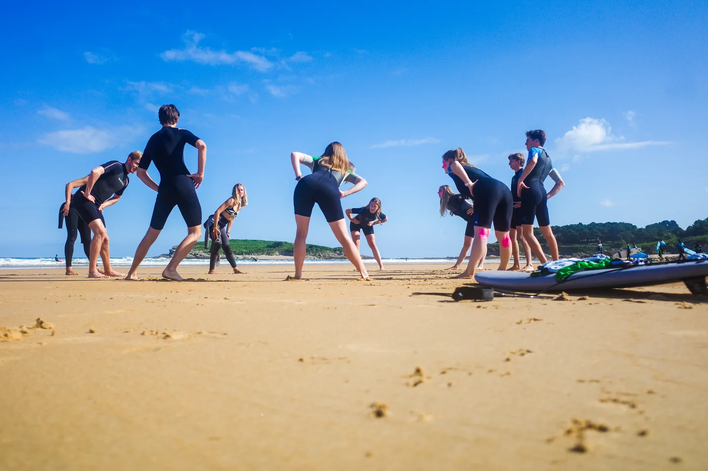 Cantabria Surfbase Loredo : Gruppe, Surf Stunde warm-up Ein Gruppe von young surfers in wetsuits performs stretching exercises auf ein sandig Strand in Cantabria, mit surfboards visible nearby.