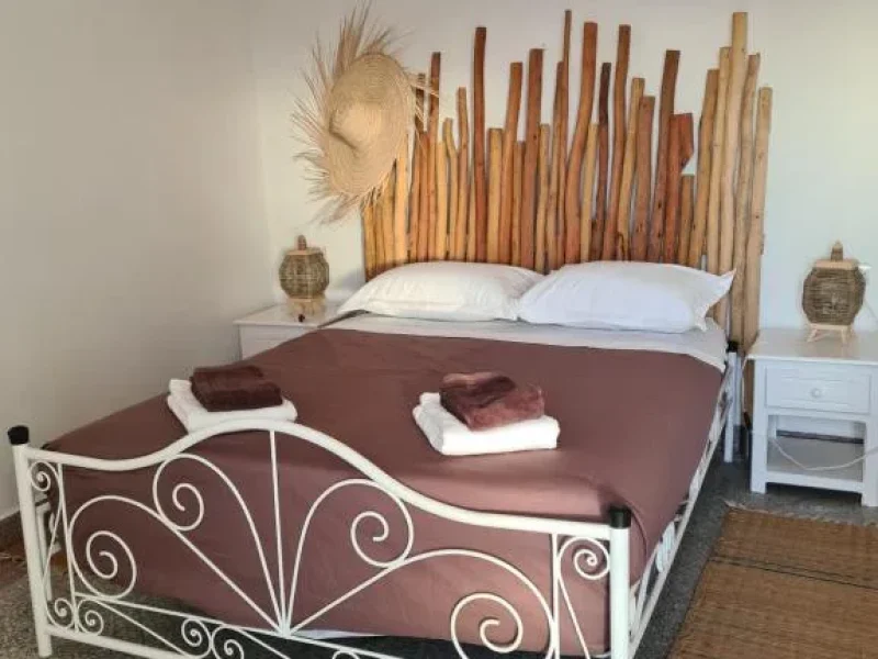 Chambre à Holy Beach House présente un lit double avec cadre métallique blanc orné, literie bordeaux, art mural en bambou en tête de lit et suspension tissée.