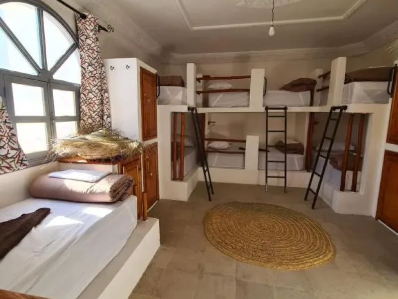 Chambre dortoir partagée multi-lits à Holy Beach House avec lits superposés en bois, oreillers blancs et un tapis tissé à Sidi Kaouki, Essaouira.
