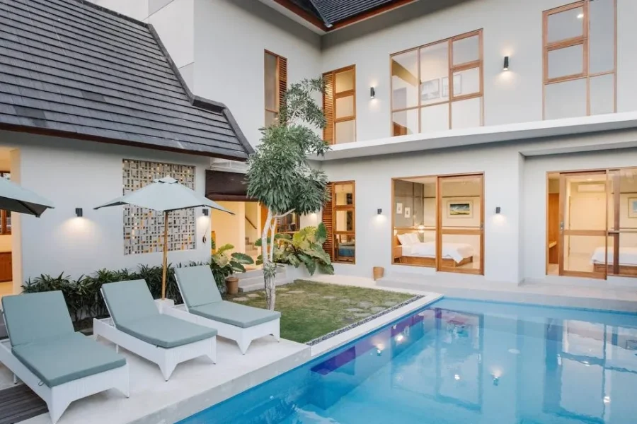 In Da Surf Bali's central courtyard features a swimming pool with lounge seating, manicured lawn, and modern architecture with wooden-framed windows overlooking the space.
