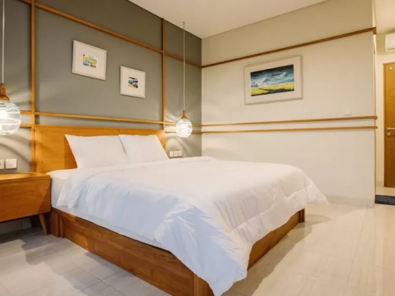 Private double room at In Da Surf Bali featuring a wooden bed frame, white bedding, pendant light, and framed artwork on walls.