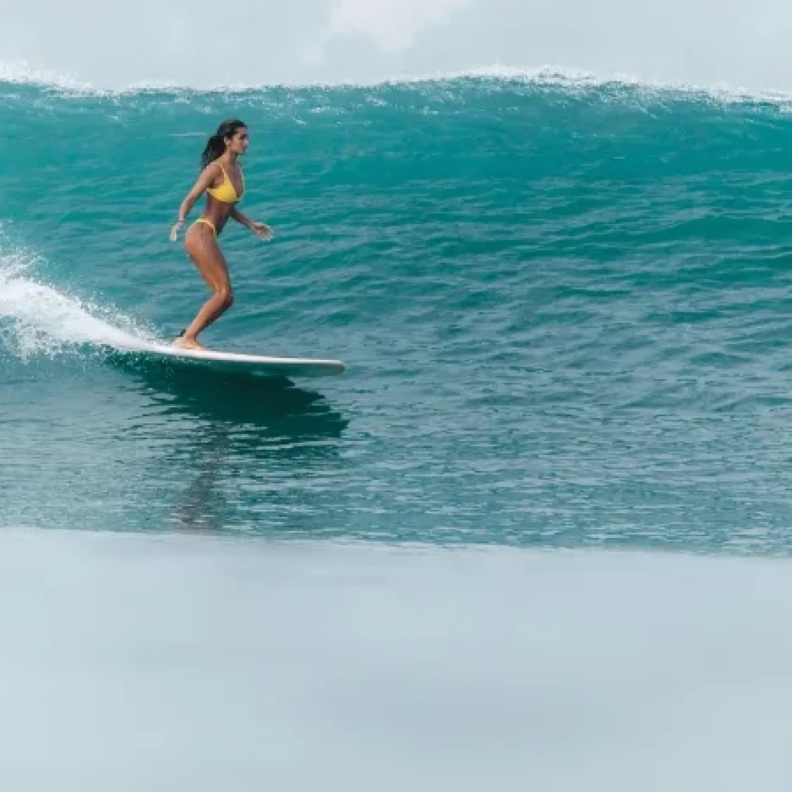 Surfeuse glissant sur une vague en eau turquoise à Canggu, Bali.