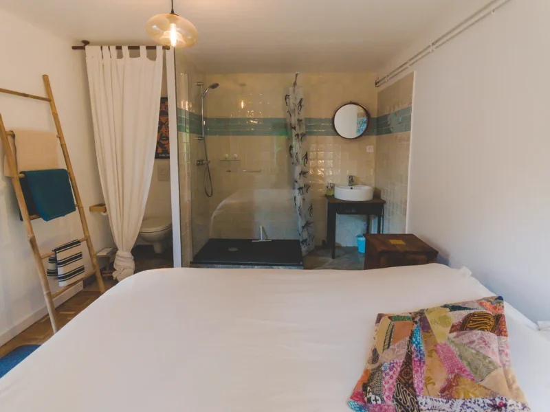 Double room with white bed and glass-enclosed walk-in shower with decorative tile accent at Joyu Surf House in Bidart.