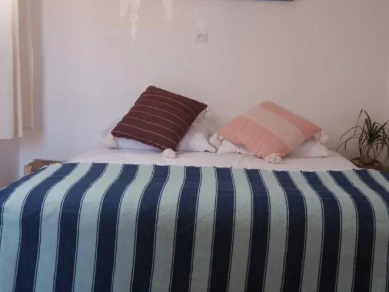 Chambre privée avec literie rayée bleue et blanche, oreillers décoratifs et murs blancs avec un cadre de fenêtre bleu.