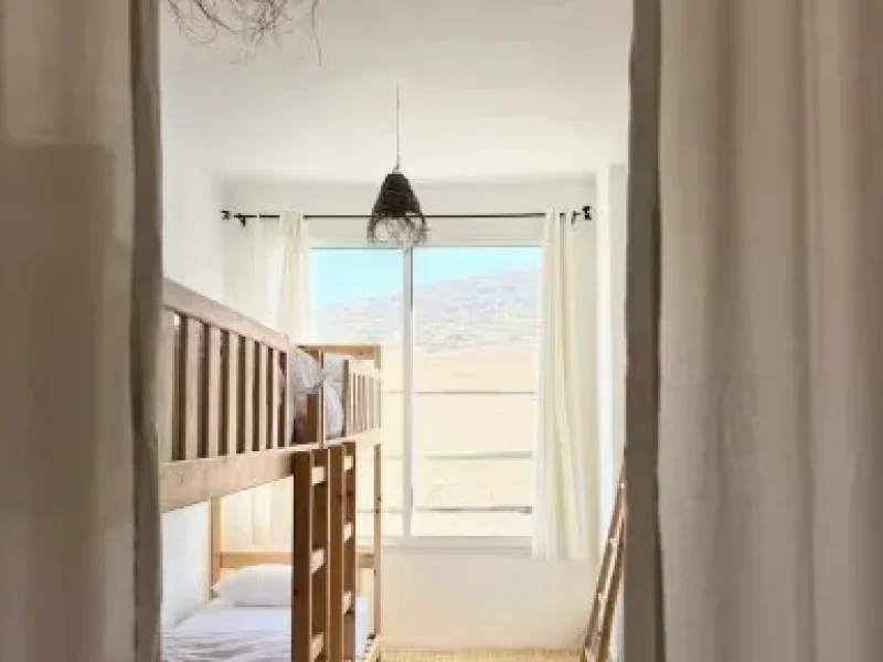 Chambre partagée avec lit bébé en bois et portes vitrées s'ouvrant sur la terrasse surplombant la plage d'Imsouane.