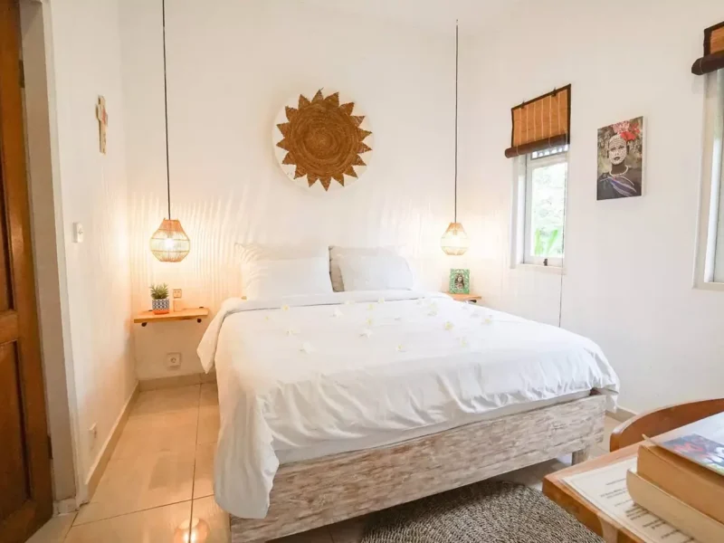 Private double room at Mondo Surf Village features a wooden bed frame with white linens, pendant lighting, and decorative wall art.