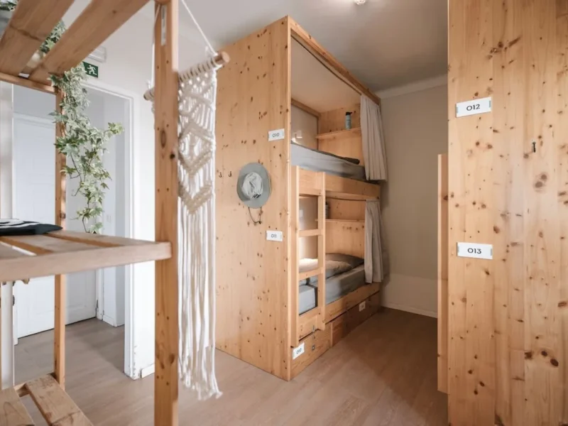 Mehrbett-Schlafsaal aus Holz mit einzelnen abgeschlossenen Bett-Kabinen und nummerierten Zimmerschildern im Surfbase Lisbon.