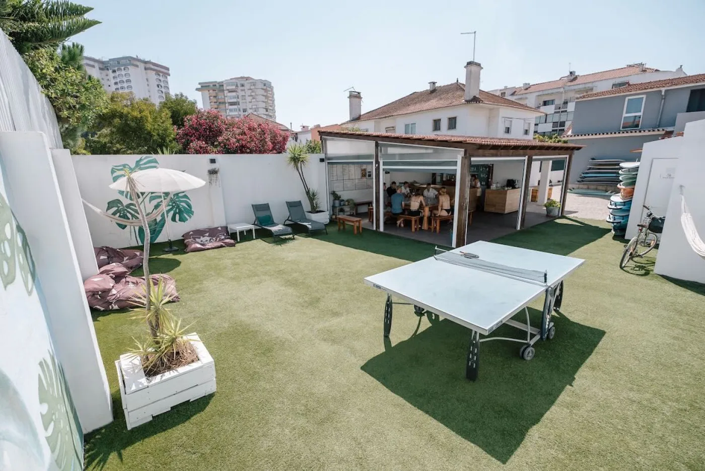 Dachterrasse von Surfbase Lisbon mit Open-Air-Dining-Pavillon, Tischtennisbereich, Holzdeck-Sitzgelegenheiten und Blick über die Skyline von Lissabon.