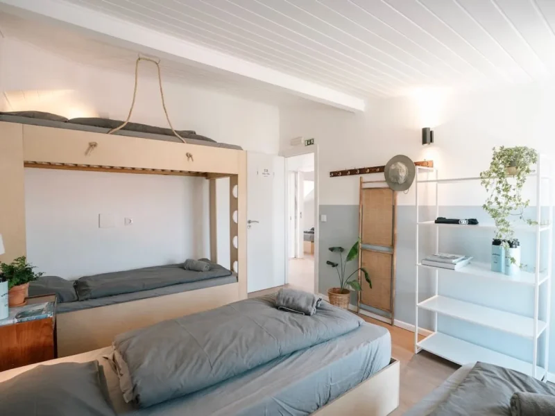 Privates Vierbettzimmer im Surfbase Lisbon mit Etagenbett aus Naturholz, grauen Matratzen und weißen Regalen.