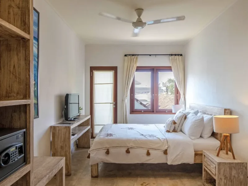 Deluxe bedroom at Soleia Surf Canggu with wooden furniture, ceiling fan, and beach view through red-framed doors.