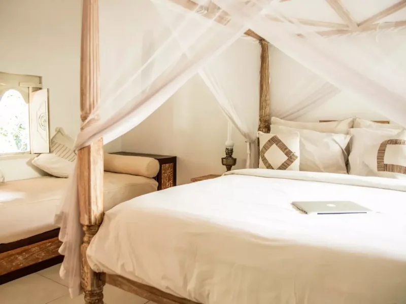 Private triple room at Mondo Surf Village features a wooden four-poster canopy bed with white draped curtains and neutral furnishings.