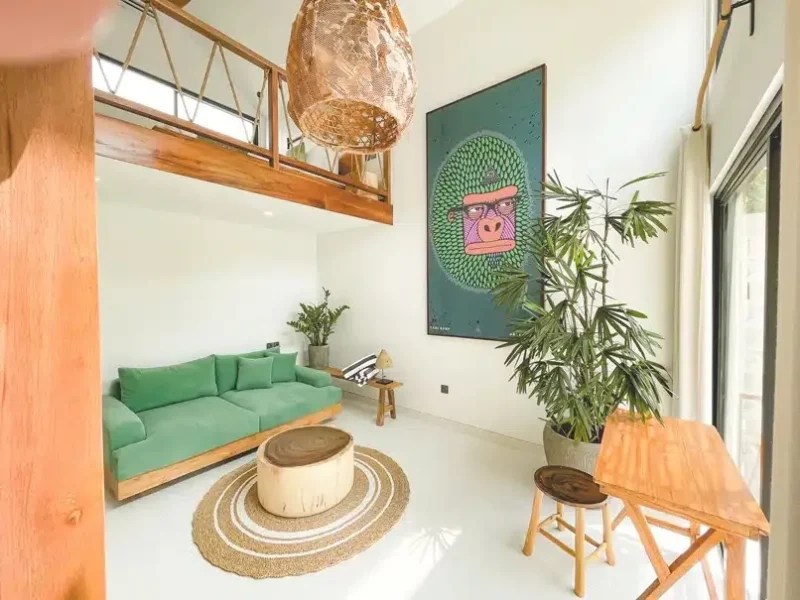 Mezzanine studio interior with green sofa, woven lamp fixture, plant decor, and contemporary artwork on wall.