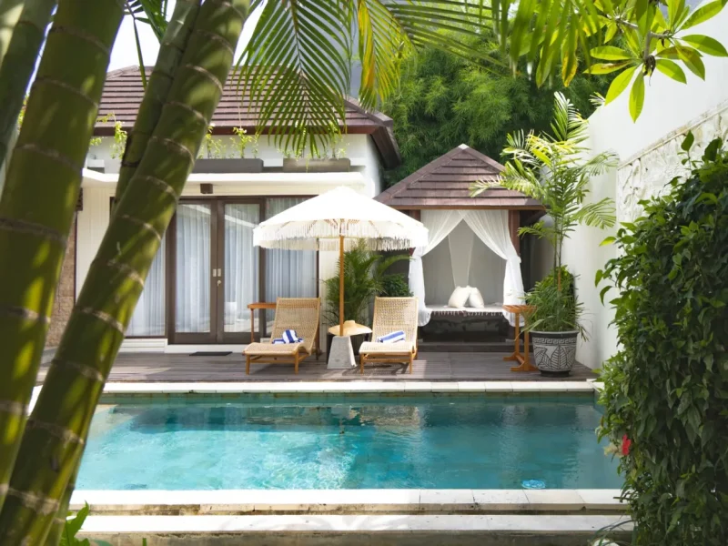 Private villa pool deck featuring loungers, white umbrella, and gazebo with surrounding tropical vegetation in Uluwatu.