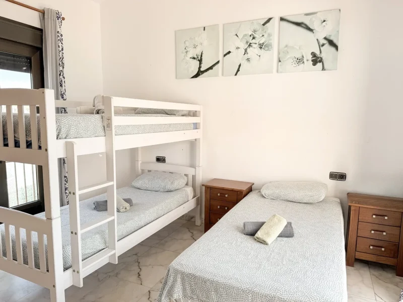 Damen-Gemeinschafts-Schlafzimmer in der International Surf School mit weißem Etagenbett, Einzelbett und minimalistischem Dekor.