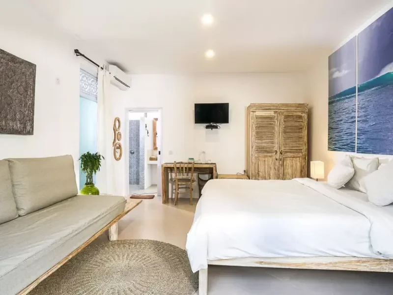 Private triple room at Mondo Surf Village in Canggu featuring a bed with white linens, wooden wardrobe, seating area, and ensuite bathroom.