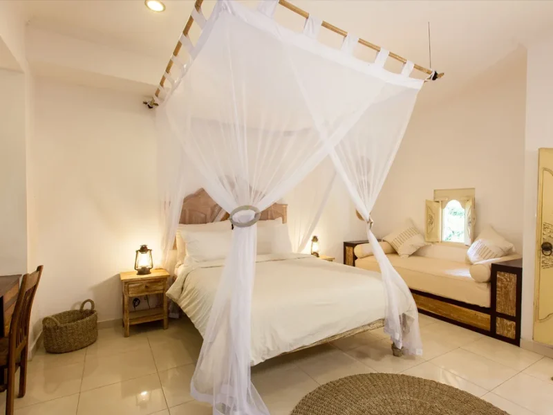 Merapi private triple room featuring white four-poster canopy bed with flowing white drapes, wooden nightstands and warm lighting.