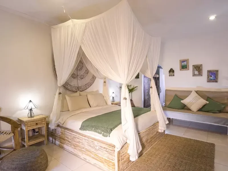 Semeru private bungalow bedroom in Canggu with wooden four-poster canopy bed draped in white sheer fabric and green throw blanket.