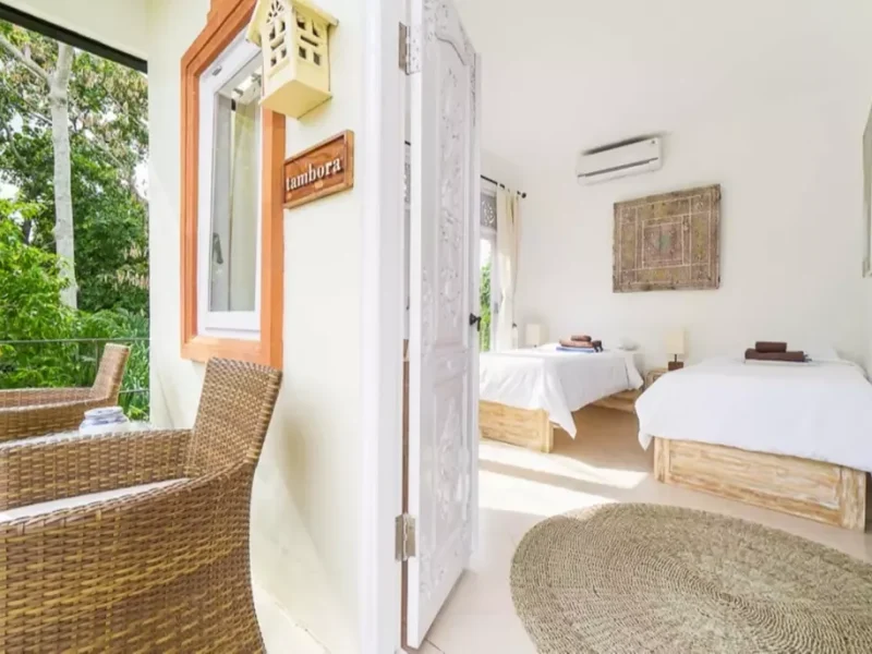 Tambora private double room at Mondo Surf Village features wooden beds with white linens, woven chairs, and white walls with natural light from windows.