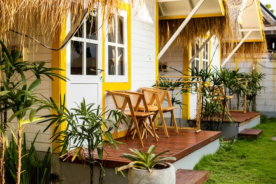 Soleia Surf Canggu terrace featuring wooden chairs, white-trimmed doors, yellow trim, and tropical plants.