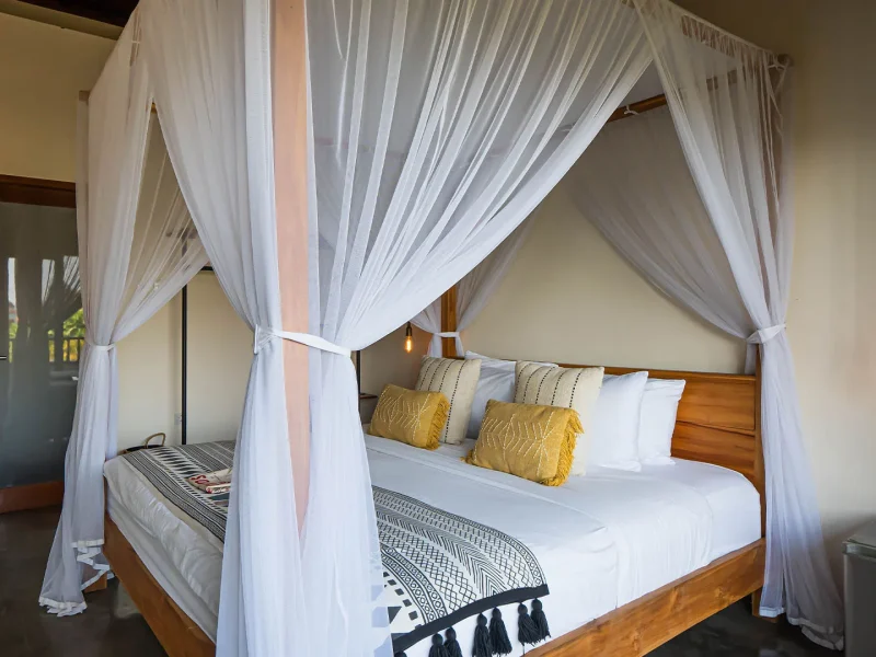 Superior Room at Soleia Surf Canggu features a wooden canopy bed with flowing white curtains and gold accent pillows.