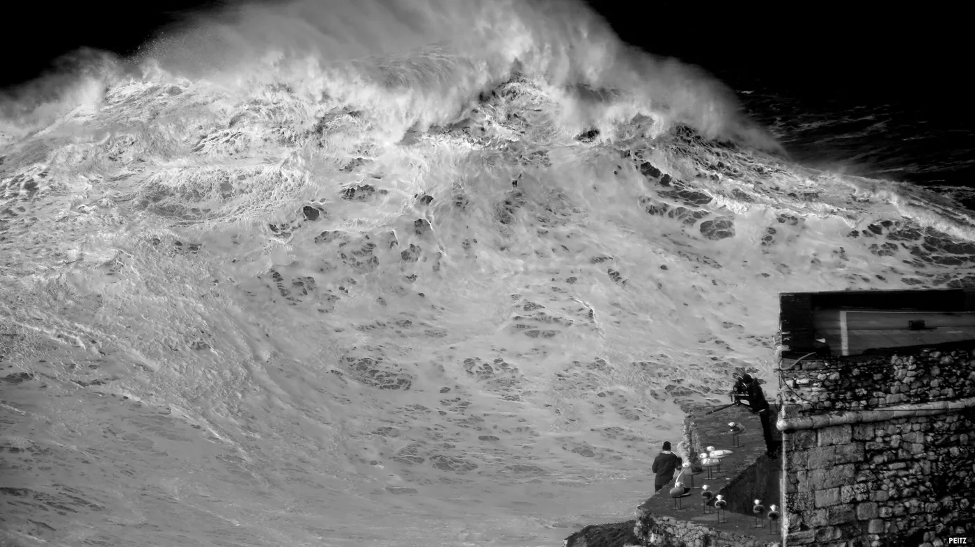 Eine massive Atlantikwelle bricht an Praia do Norte in Nazaré, Portugal, und zeigt die dramatische vertikale Wand, die der Unterwasser-Nazaré-Canyon erzeugt.