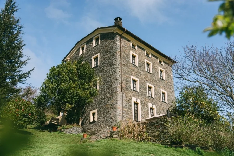 Edificio a torre in pietra presso il camp Enjoy Native nelle Asturie con motivi regolari di finestre, paesaggio verde circostante e vegetazione consolidata.