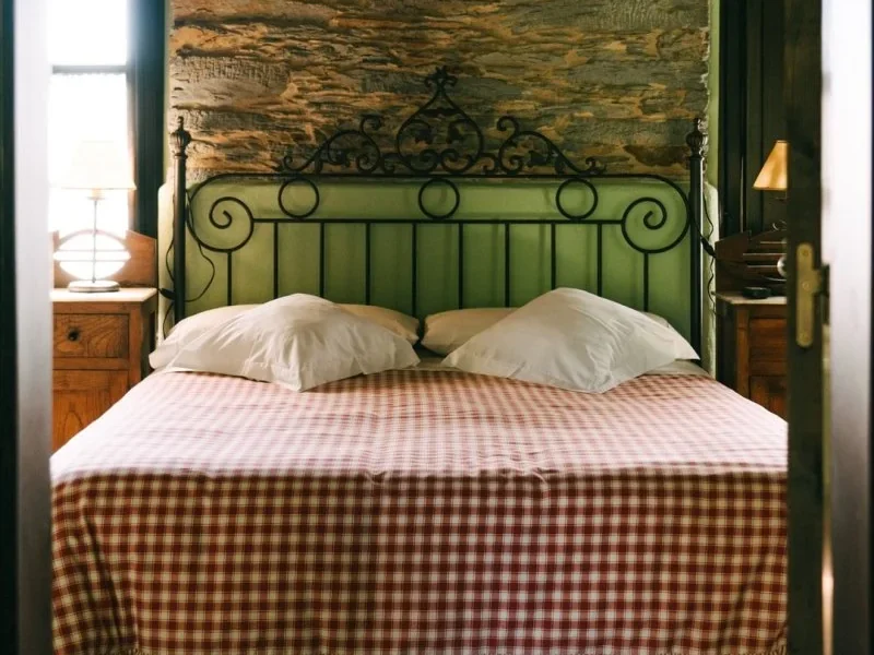 Private single room at Enjoy Native camp featuring a wrought iron four-poster bed with white pillows and checked bedding, wooden walls, and traditional furnishings.