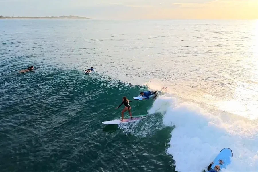 Three surfers riding and paddling in waves at Arugam Bay with a coastal island visible in the background at sunrise.
