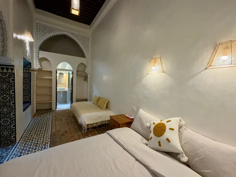 Family room bedroom at Ilyana Surf House in Rabat features two beds with white linens, yellow cushions, and Moroccan architectural elements including arched doorway.