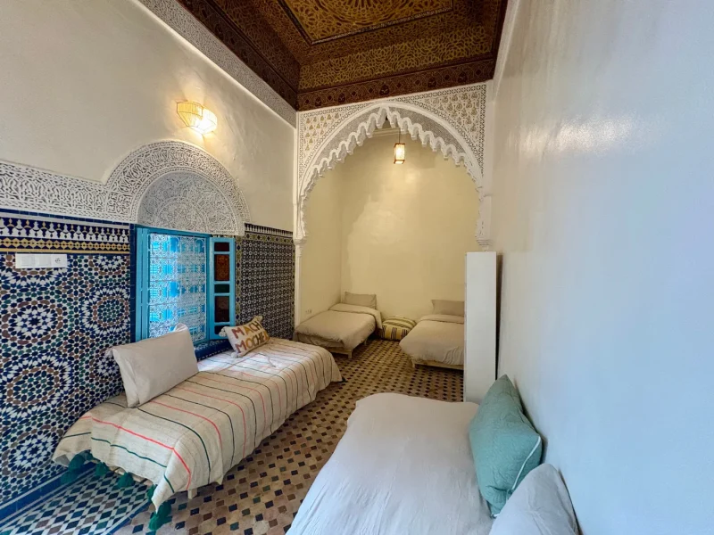 Shared room at Ilyana Surf House in Rabat with multiple beds, arched alcove niche, and traditional Moroccan zellige tilework.